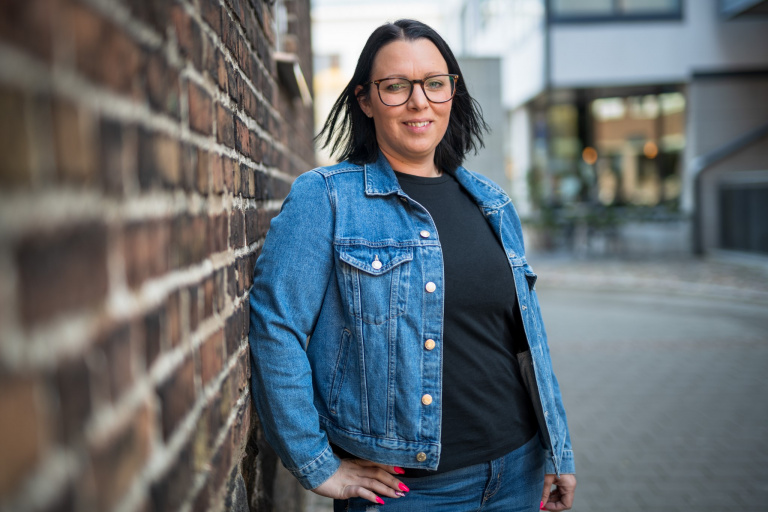 Kvinna står lutad mot en tegelvägg.
