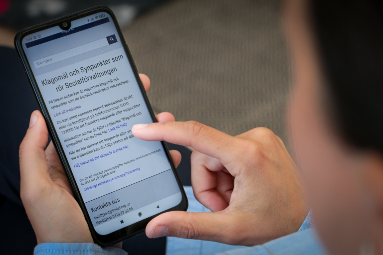 Person sitter med mobiltelefon i sin hand.