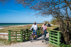 Två personer cyklar på en grusstig längs havet.