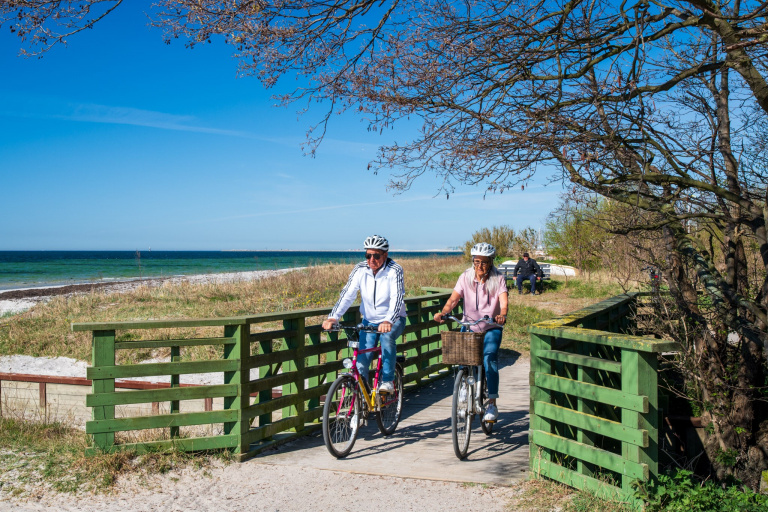 Två personer cyklar på en grusstig längs havet.