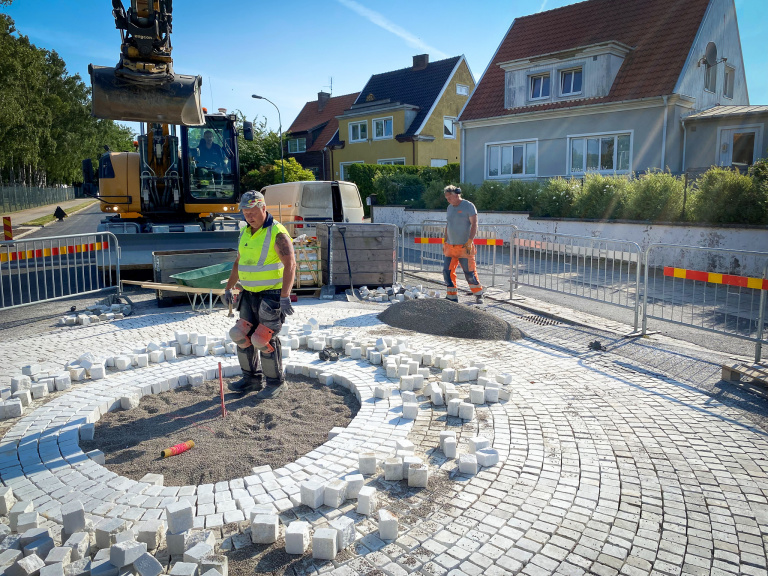 Gatuarbetare och grävskopa vid pågående beläggningsarbete