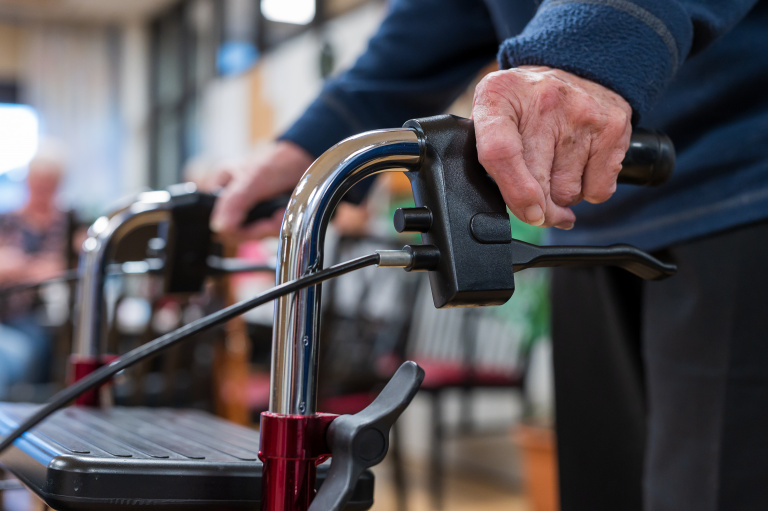Två händer håller i handtag till rollator.
