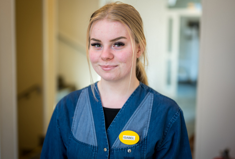 Kvinna i arbetskläder ler och tittar in i kameran.
