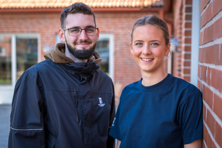 Man och kvinna står utomhus intill husvägg.