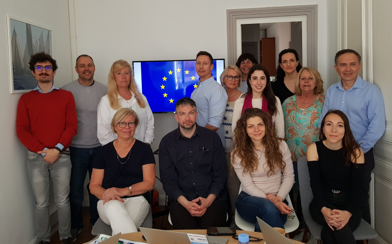 Grupp personer sitter och står i ett rum med EU-symbol i bakgrund.