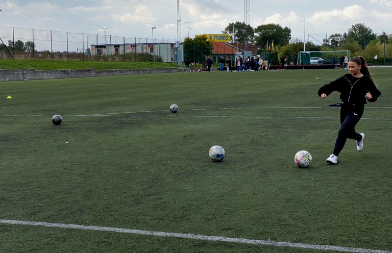 Flicka på fotbollsplan som skjuter iväg fotboll
