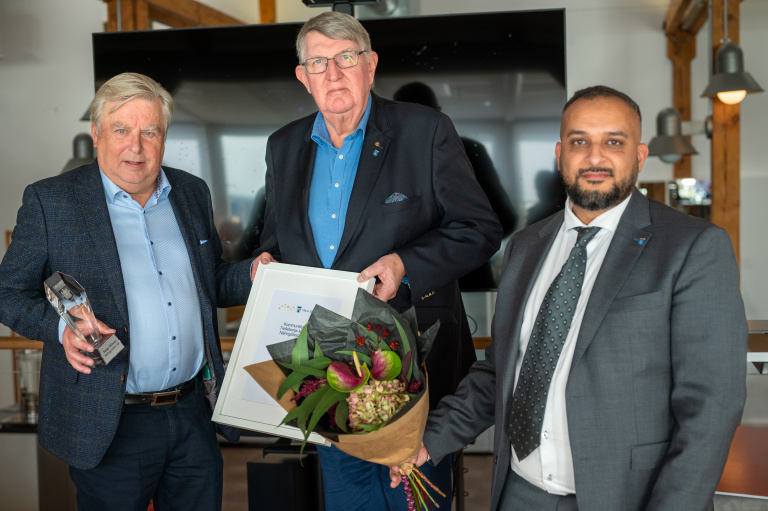 Tre män med blommor och diplom i händerna