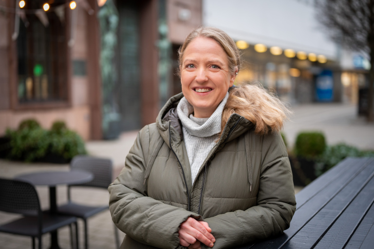 Kvinna står utomhus och ler in i kameran.