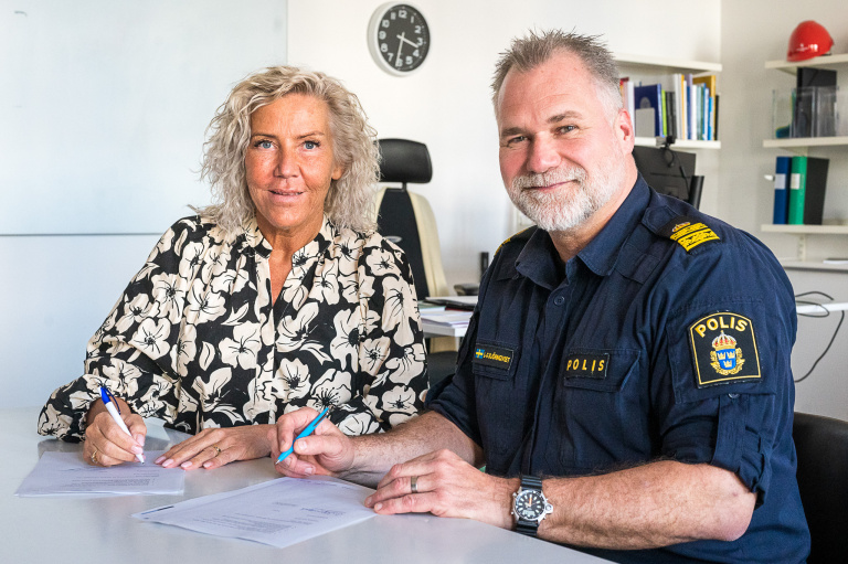 Två personer sitter vid ett skrivbord för att skriva på ett dokument.
