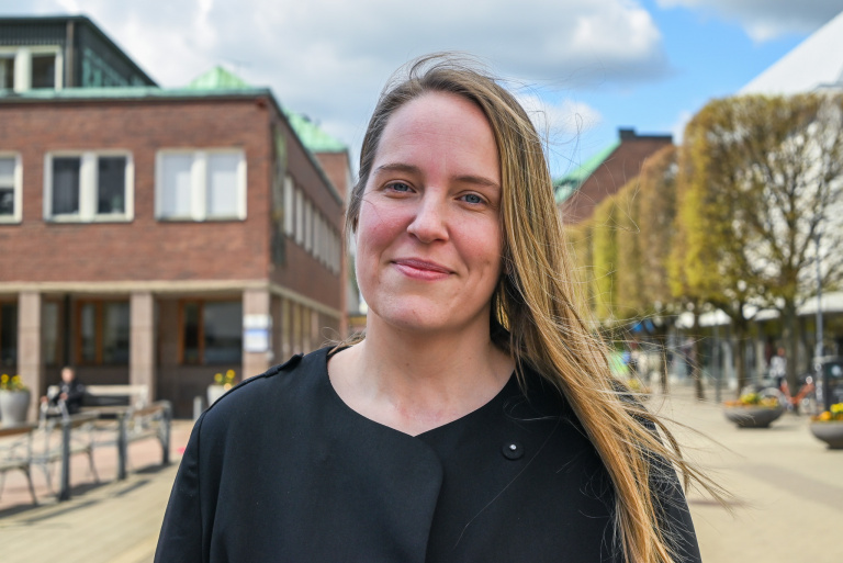 Kvinna står ute på en gata och tittar in i kameran.