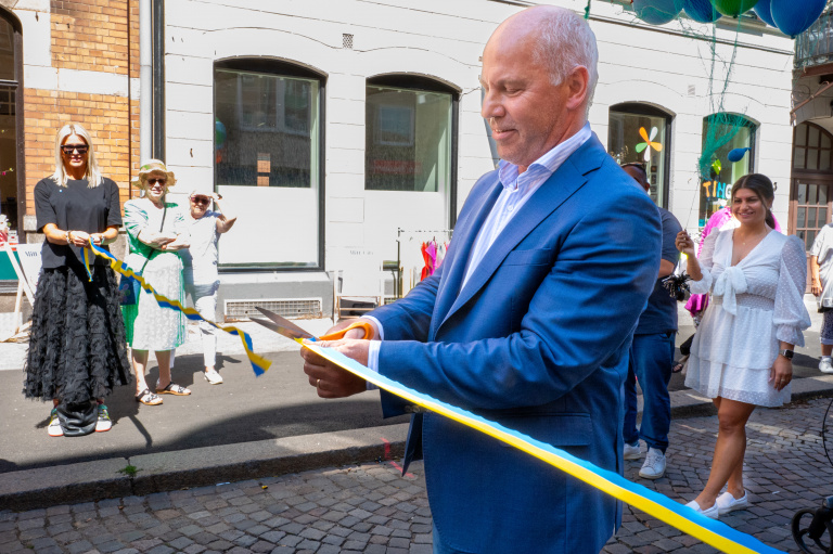 Man i kostym som klipper ett gult och blått band