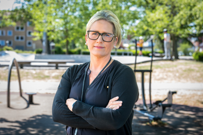 Svartklädd kvinna med glasögon står med armarna i kors med skatepark i bakgrunden.