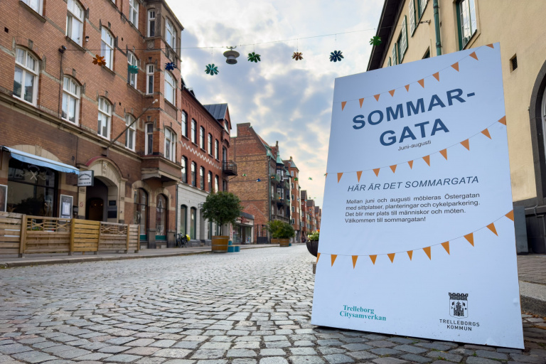 Kullerstensgata, husfasader i rött tegel, skylt med information om sommargata.