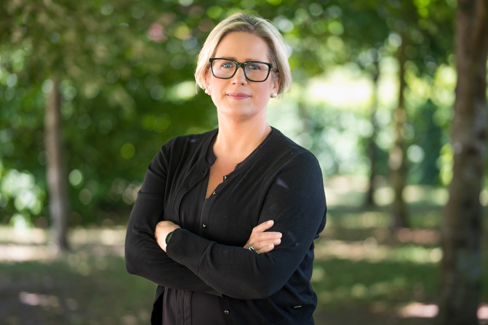 Kvinna står med armar i kors i en park.