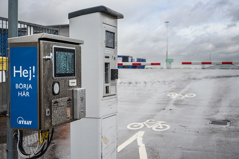 Asfalterad infart till återvinningscentral med bom och automat för avläsning av körkort