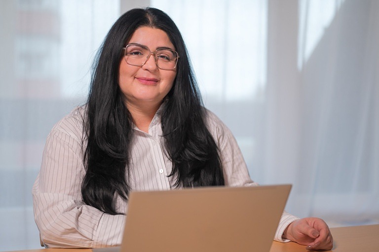 Kvinna sitter vid datorskärm och ler in i kameran.