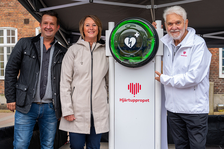 Hasse "Kvinnaböske" Andersson inviger Trelleborgs kommuns nya hjärtstartare tillsammans med kommundirektör Gisela Öst och TrelleborgsHems fastighetschef Ricardo Klemensson.