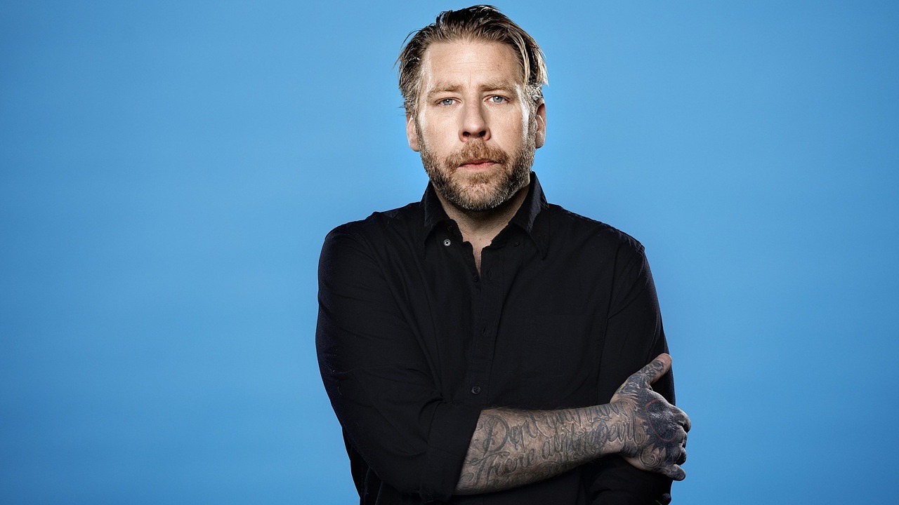 man i svart skjorta mot blå bakgrund