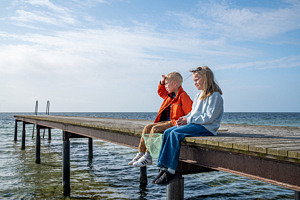 Foto på två barn som sitter på en brygga och spanar utåt horisonten.