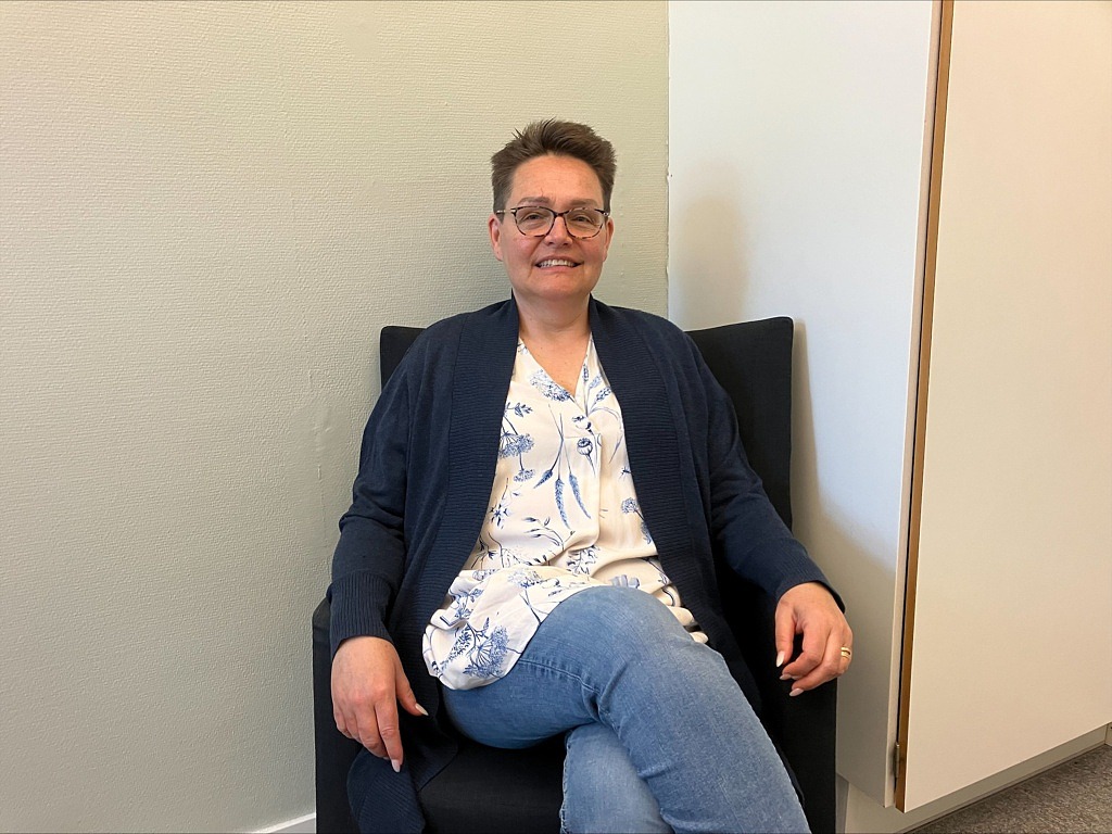 Kvinna sitter i fåtölj och ler in i kameran.